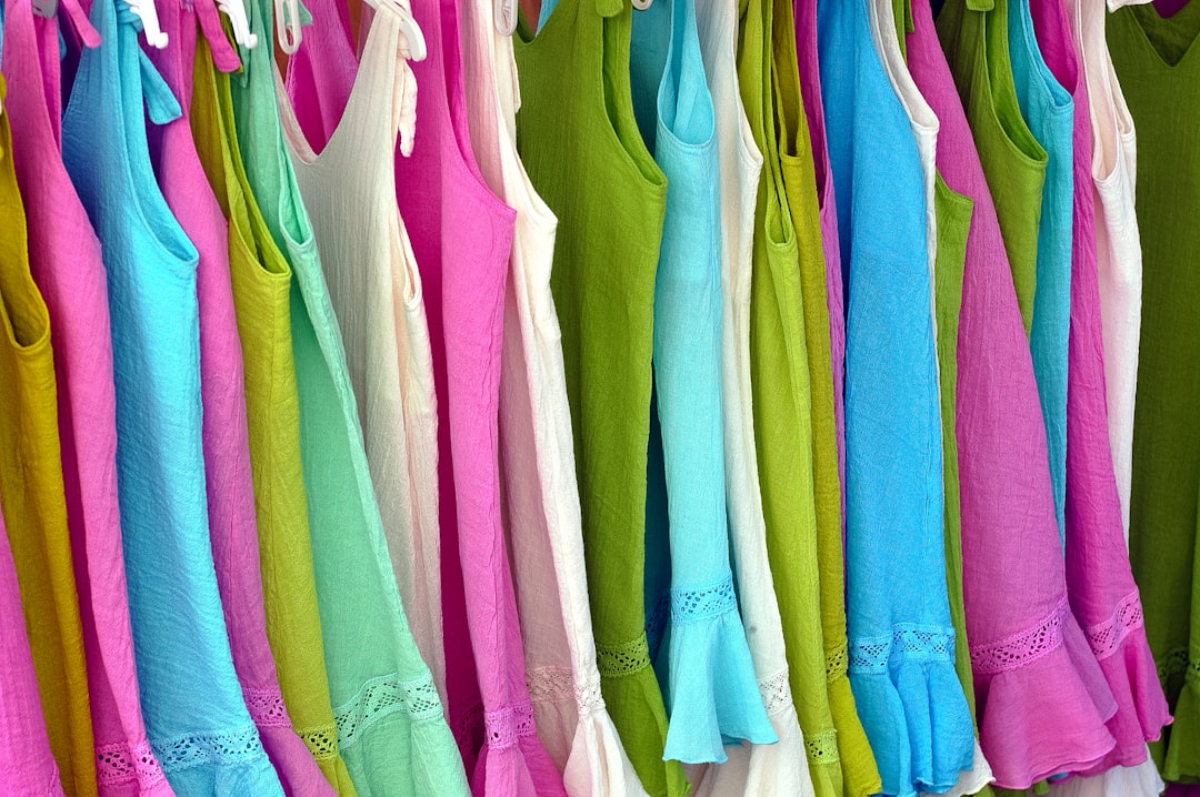 Colorful summer dresses on hangers in shades of pink, blue, green, and white displayed in a fashion boutique or clothing store.